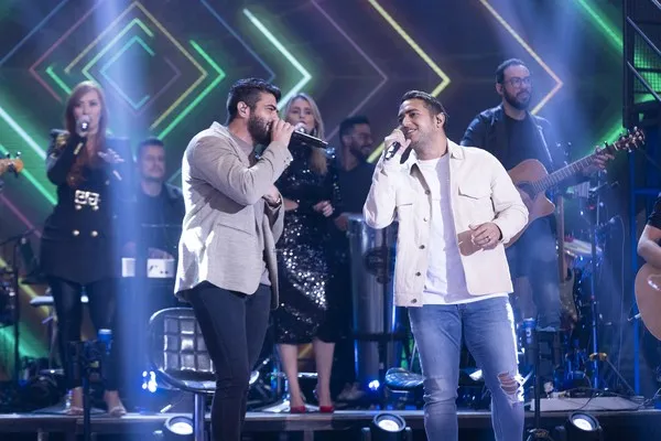 Henrique e Juliano singing on stage, with the band behind them.